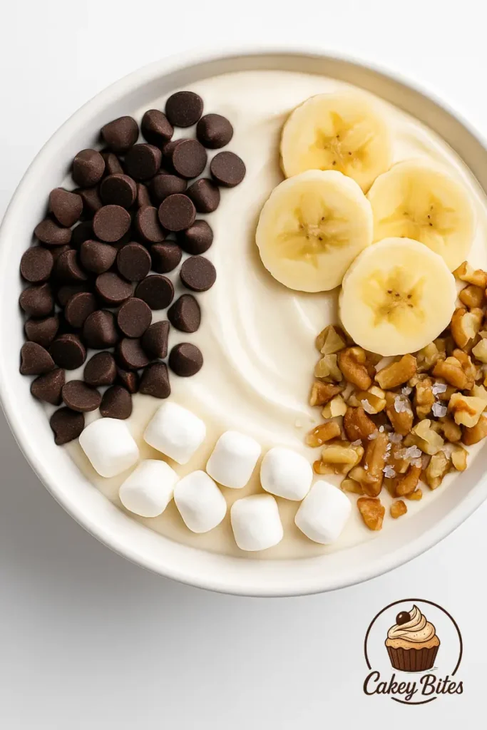 Toppings for brownie lover’s peanut butter pizza—chocolate chips, bananas, walnuts, and marshmallows for a creative dessert twist. A dessert bowl styled with chocolate chips, banana slices, chopped nuts, and mini marshmallows—ideal topping inspirations for a brownie lover's peanut butter pizza.